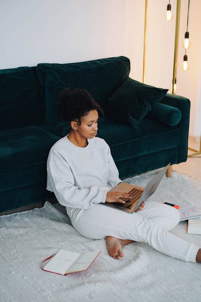 Black woman sitting on floor using laptop for online learning at home.
